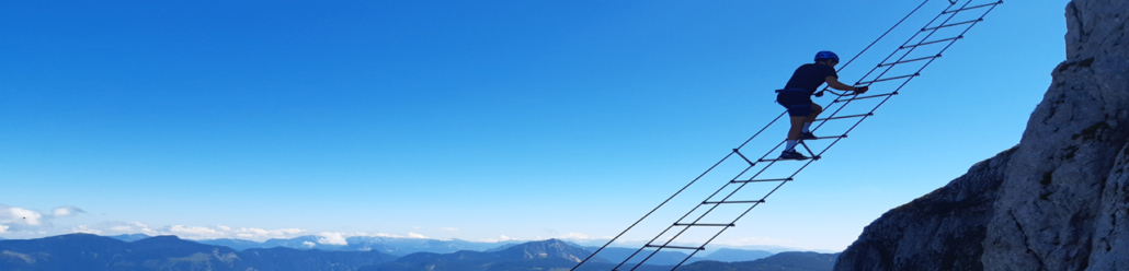 Ein Klettersteiggeher auf der frei hängenden Himmelsleiter vor blauem Himmel